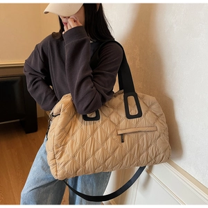 Detail of khaki quilted tote bag featuring a diamond pattern and black reinforced handles