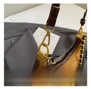 Detail of golden metal hook on brown crocodile embossed leather and suede crossbody bag