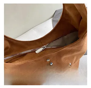 Detailed close-up of brown suede hobo bag with silver metal zipper and rivet accents
