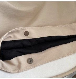 Detailed macro view of the magnetic closure and fine stitching on the beige fabric tote bag