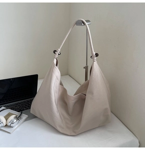 Close-up of cream Hobo bag with knotted rope strap and brown spherical detail on desk