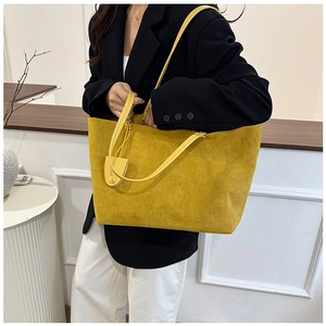 Detail of yellow suede tote bag with shoulder straps and decorative charm on model