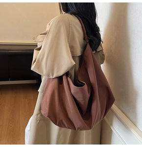 Detail view of large red-brown canvas shoulder bag with wide knotted strap on model