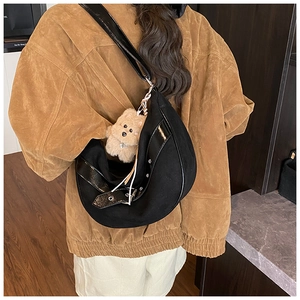 Close-up of black canvas crescent bag with metal eyelets and a plush bear charm on a model
