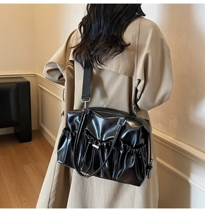 Detail of black pleated tote bag showing the side drawstring pocket and glossy PU texture