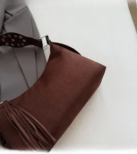 Detail of dark brown suede bag featuring long fringe tassels and silver stud strap hardware