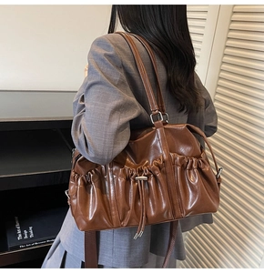 Sac fourre-tout en cuir marron caramel avec plis portés sur une veste à carreaux gris