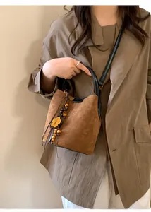 Close-up of brown suede bucket bag with yellow floral charm and black leather handle