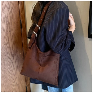 Close-up of retro brown suede tote bag featuring adjustable metal buckles and outer pocket