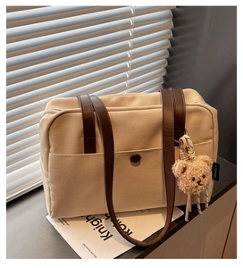 Detail of canvas tote bag with brown leather straps and cute beige plush bear pendant