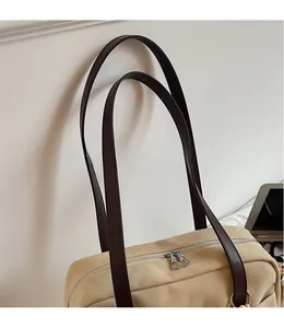 Close-up of beige canvas tote bag with smooth brown leather shoulder strap and metal zipper