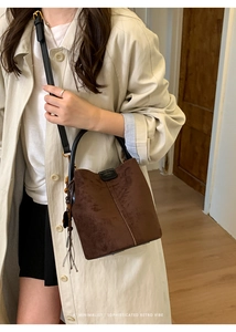 Detail of dark brown suede bucket bag with leather handles and tassel bead charm