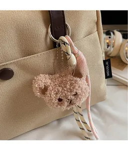 Detail of a brown teddy bear plush keychain with woven knots on a canvas bag handle