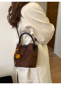 Detailed view of brown suede bucket bag with ethnic charms and leather handle on a model