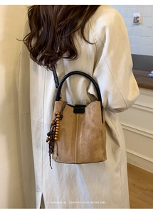Detailed macro view of a brown suede bucket bag featuring elegant wooden bead tassels