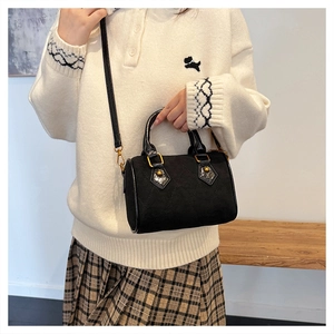 Detalle del bolso cilíndrico acolchado negro mate con herrajes dorados y asa superior