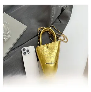 Macro detail of mini gold bucket bag with crocodile texture and metallic round handle