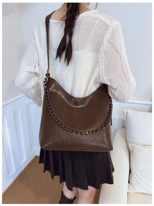 Close-up of a deep brown bucket bag with shiny faux leather finish and chunky chain detail