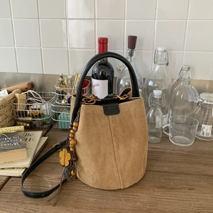 Detailed close-up of brown suede bucket bag with wooden flower pendant and black handles