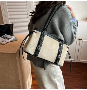 Detail view of large canvas tote bag with black leather straps and metal buckle accents