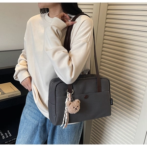 Detail of dark grey canvas tote with brown straps and cute plush bear charm on model