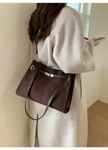 Detail of dark brown suede tote bag with silver metal clasp worn on shoulder