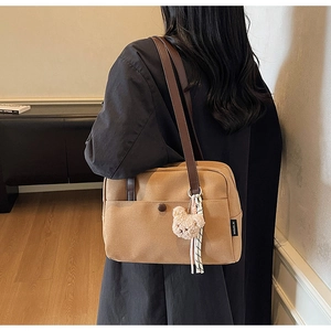 Detail of khaki canvas bag with brown leather strap and plush bear charm decoration