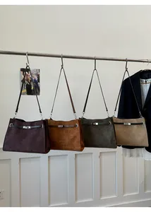 Detail of four suede crossbody bags in dark purple, brown, green and sand hanging on a rack