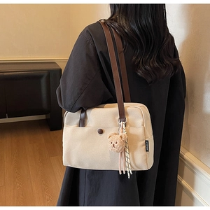 Detail of canvas tote bag showing beige texture, leather strap, and cute bear pendant