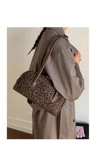 Close-up of leopard print baguette bag with brown leather handles on model's shoulder