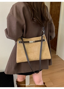 Detail of tan suede shoulder bag featuring classic strap closure and retro metal hardware