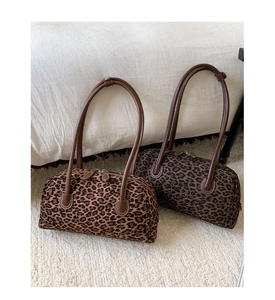Detail of leopard print boston bags with dual zippers and long handles on a beige rug