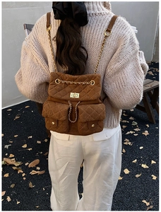 Rear view of brown quilted backpack with gold chain straps on an autumn outdoor background