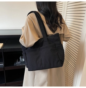 Detail of black corduroy tote bag with multiple pockets worn over a beige trench coat