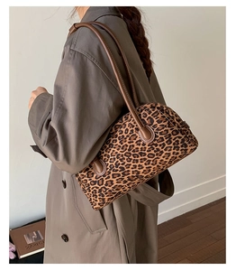 Detail of leopard print baguette bag with brown leather strap worn over a brown coat