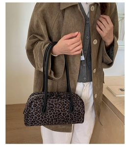 Detailed view of leopard print baguette bag with black leather shoulder straps on a table