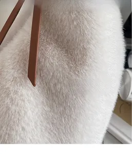 Détail de la texture pelucheuse et de la bandoulière en cuir brun du sac blanc