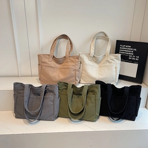 Minimalist corduroy tote bags in multiple colors with large front pockets on a white stand