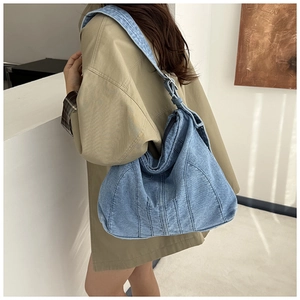 Detail van de vintage denim hobo tas met stiksels gedragen over een kaki trenchcoat
