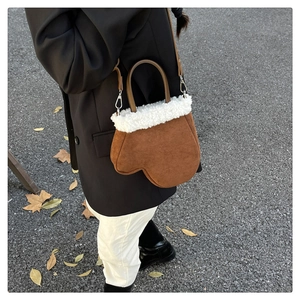 Detailed shot of brown suede glove-shaped handbag with plush white faux fur trim and strap