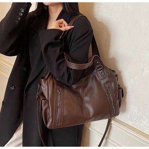 Detail of dark brown leather tote bag with grainy texture and functional metal zippers