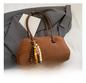 Dettaglio borsa tote in pelle scamosciata marrone con nappa etnica su un blazer grigio