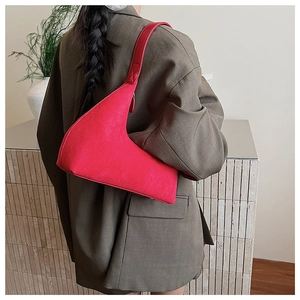 Detail view of red suede asymmetrical shoulder bag showing soft texture and modern curved shape