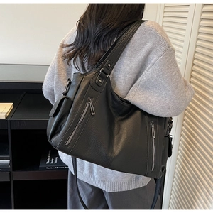 Close-up of black lychee grain leather tote bag with functional side pockets and zippers