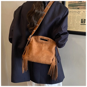 Close-up of brown suede crossbody bag featuring retro bohemian tassels and metal eyelets