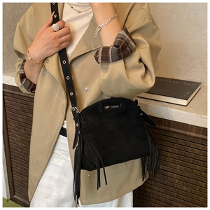 Close-up of black suede crossbody bag with fringe details and adjustable strap on a model