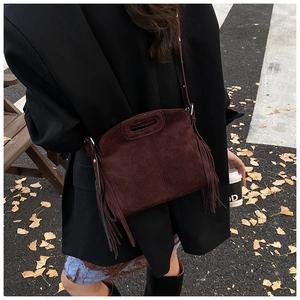 Detail shot of a dark brown suede shoulder bag with long side tassels and cutout handles