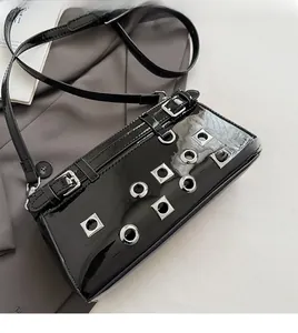 Detail of black patent leather crossbody bag with silver eyelets and metal rivet studs