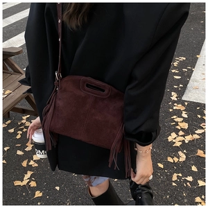 Close-up of a burgundy suede crossbody bag with fringe details and oval cutout handle