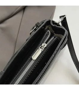 Close-up of smooth silver metal zipper detail on a black glossy leather baguette bag